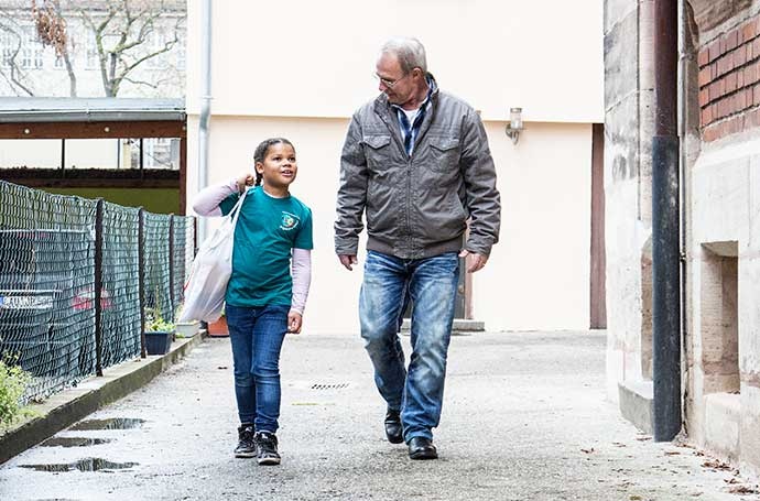 Eine junge Jugendrotkreuzlerin trägt die Einkaufstasche eines älteren Mannes.